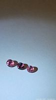 Three round cut pink-purple tourmaline gemstones placed in a row on a white background showing their size, color, and clarity.