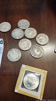 Seven silver coins on table including six Canadian silver dollars and one 1964 Kennedy half dollar in flip