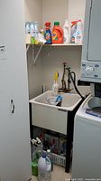 Wide view of cleaning supplies on shelf over utility sink including laundry detergent, bleach, sprays