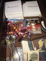 Drawer containing boxed Holland America Line coasters, assorted costume jewelry in plastic bag, and kitchen napkin rings.