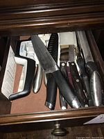 Photo of drawer showing multiple knives with black and wooden handles, and a knife sharpener.