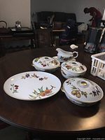 Full view of nine-piece Royal Worcester Evesham serving set on table, showing gravy boat, lidded serving dishes, and serving plates with fruit and leaf patterns and gold trim.