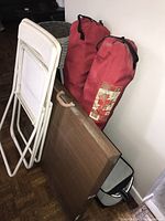 Photo showing plastic white folding chair, two red camping chair bags, and wood grain folding table.