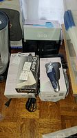 Photo showing QUO electric shaver box in blue and black, Dynasty hair dryer packaging and other boxed hair appliances.