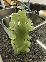 Front view of the green jade figurine showing the woman holding a flower and detailed floral elements.