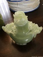 Front view of the jade vessel showing pale green color and detailed dragon carvings on handles and lid.