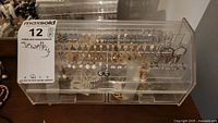 Front view of clear acrylic jewelry organizer showing two rows of hanging earrings and closed drawers
