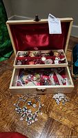 Wooden jewelry box open showing red velvet lined compartments filled with assorted costume jewelry