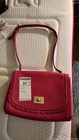 View of the front of the pink purse showing scalloped flap and gold-tone clasp with maxsold tag