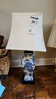 Full view of blue and white ceramic lamp with square white fabric shade and visible cord.