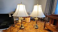 Pair of matching brass lamps with beige fabric shades sitting on parquet floor near furniture.