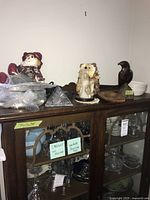 Wide view of cabinet top with multiple decorative items including the stone carving sculpture, wooden eagle bust, decorative stuffed animal, and rag man, plus trays and ceramic bowls.