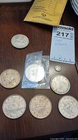 Overhead shot showing seven silver dollar coins and one dime with lot tag