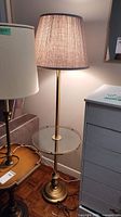 Floor lamp showing brass base, pole, glass table, and beige fabric lamp shade
