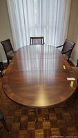 Front view of oval mahogany dining table with two leaves and chairs in background.