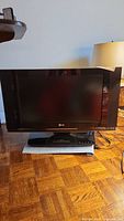 Front view of LG 23 inch TV on stand with a lamp and wooden floor visible