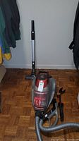 Front angled view of red and gray Bissell Multi-Surface Expert upright vacuum with hose and attachments laid out on floor.