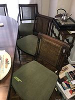 Photo showing three vintage dining chairs with medium green upholstered seats, cane backs and wooden frames, positioned beside a dining table.