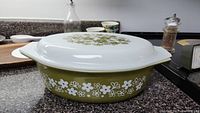 Side view of vintage Pyrex Spring Blossom casserole dish showing olive green floral pattern on white glass and side handle