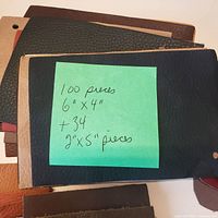 Leather sample swatches arranged in stacks, showing the various colors and textures including black, brown, tan, grey, and white. A note with quantity and dimensions is placed on top of one stack.