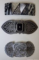 Three different hair clasps: One rectangular hair clasp with black and white geometric patterns; one engraved metal oval hair clasp with filigree, black and rhinestone center; one rectangular clasp with mixed patterns and rhinestones.