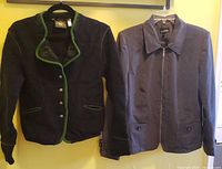 Two waist length ladies jackets hanging on wall, one green embroidered wool Hammerschmid and one grey zip-up Lindor