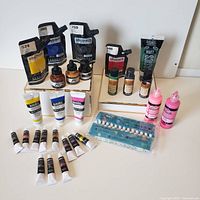 Overview of crafting paints in tubes, squeeze bottles, and liquid drop bottles arranged with a color shade guide.