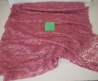 Photo showing folded piece of sheer pink lace fabric spread out on a flat surface with intricate floral lace patterns visible.