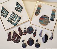 Overview of handcrafted polymer earrings and pendants array on white background, showing multiple shapes and colors.