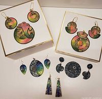 View of multiple pairs of handcrafted polymer earrings and pendants arranged on a white flat surface, showing various colorful and textured designs.