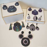 Top view showing various polymer jewelry sets arranged on white boxes including hexagonal, circular, fan-shaped earrings, and a necklace with intricate embossed and marbled patterns.