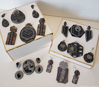 Photo showing multiple pieces of handcrafted polymer clay earrings and pendants arranged in sets on white surface with gold trim edges.