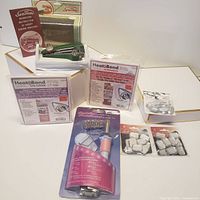 Image showing SenTon hand held stitching device with instruction booklet, two Heat Bond adhesive packages, Crystalizer accessory kit, and fabric adhesive pieces.
