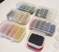 Overview image showing five clear plastic containers filled with various small colored beads in compartments and one small square container filled with black beads.