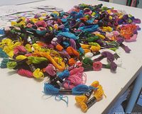 Multiple skeins of colorful craft threads spread out on a white surface, showcasing variety of colors and small size skeins with labels.