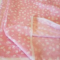 Close-up of fabric showing white leaf pattern on light pink background, showing detail of pattern and fabric texture.
