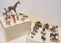 Two-tier display of various miniature plastic wild and farm animals including giraffe, tiger, lion, zebra, deer, gorilla, rhinoceros, cow, chicken, goat, and pig.