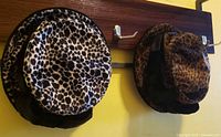 Two velvet animal print cloche hats on wall hooks, showing front and back views