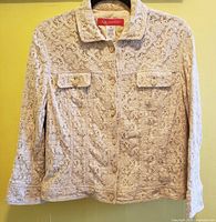 Front view of beige embroidered lace jacket with flap pockets, buttons, and collar.