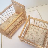Wooden 1:12 scale crib and playpen dollhouse furniture with floral-pattern mattresses shown from one angle.