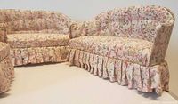 Vintage floral upholstered dollhouse sofa and loveseat side by side showing ruffled skirt detail.