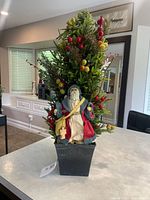 Front view of artificial tabletop Christmas tree arrangement showing Santa figurine, berries, foliage and planter