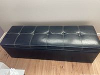 Top view of closed ottoman showing black faux leather with tufting and white stitching