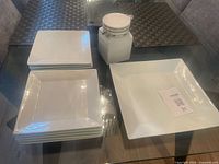 Jar, stack of small plates, and large plate on glass table