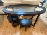 Full view of oval glass-top table with two stools underneath