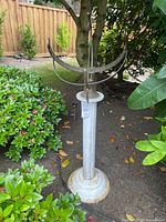 Full view of sundial on pedestal among shrubs