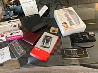 Overview of all items on table including Nikon camera, Olympus camera, skincare devices, phone accessories and wallets