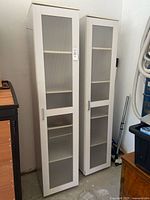 Front view of both tall white cabinets showing frosted glass doors and handles