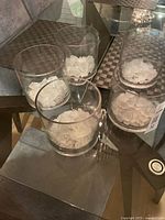 Five glass candle holders on glass table, stones visible