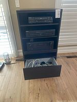 Front view of stereo cabinet showing three audio components and open drawer with cables